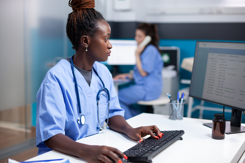 african-american-nurse-working-desk-inserting-data-appointment-table-list-concentrated-adult-woman-checking-patient-list-wearing-stethoscope-clean-modern-medical-office-operating-computer